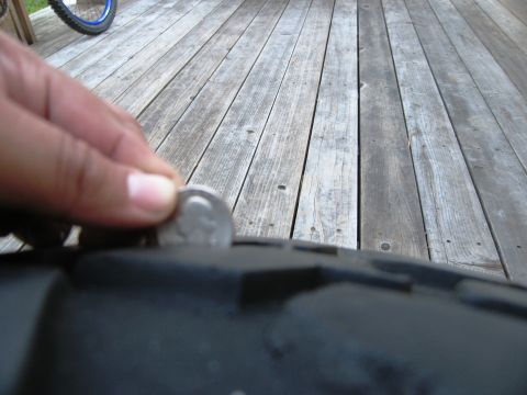 1986 Ford Bronco - A coin is used to measure the tread depth of a tire, with a wooden deck in the background.