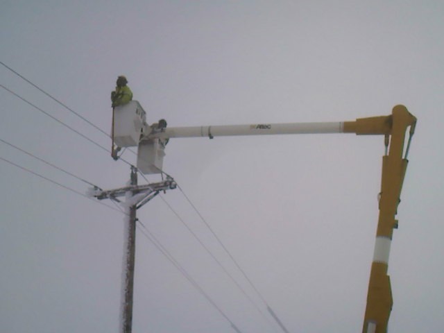 Bucket truck with two workers on power lines during a cloudy day
