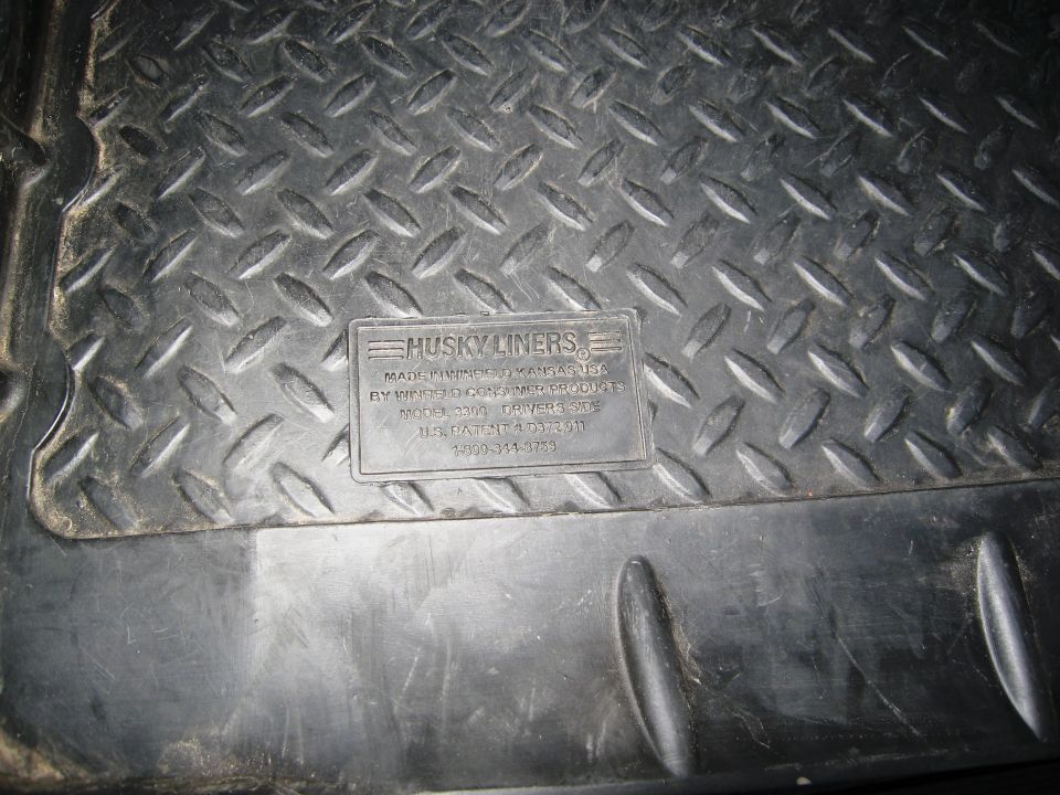 Close-up of a black diamond plate floor mat with a Husky Liners logo in the center