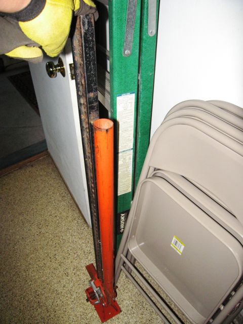 1986 Ford Bronco - A hi-lift jack and a ladder are stored indoors next to stacked chairs.