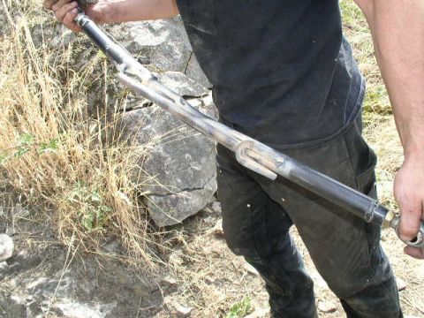 1979 Ford Bronco - A person holds a metal tie rod assembly, likely for an off-road vehicle, against a rocky, dry grass background.