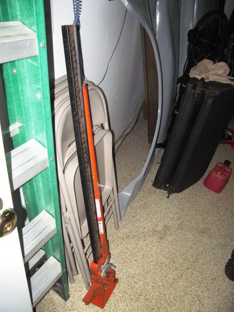 1986 Ford Bronco - A collection of items, including a hi-lift jack and folding chairs, are stored in a garage or storage area.