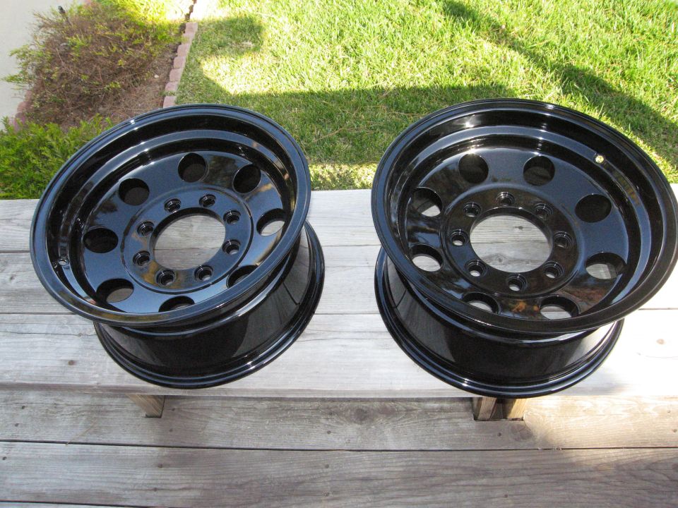 Two black steel wheels with multiple lug nut holes, resting on wooden planks