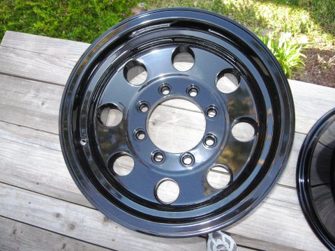 1986 Ford Bronco - A polished black wheel rests on a wooden surface, reflecting the surrounding environment.