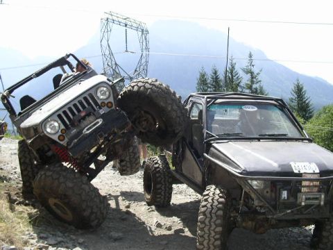 1979 Ford Bronco - Two heavily modified off-road vehicles navigate a challenging trail with steep inclines and rocky terrain.