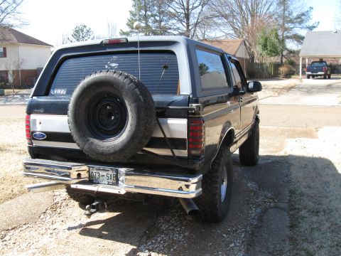 1994 Ford Bronco - Rear view of a 1994 Ford Bronco, showing the spare tire and license plate. A second vehicle is visible in the background.