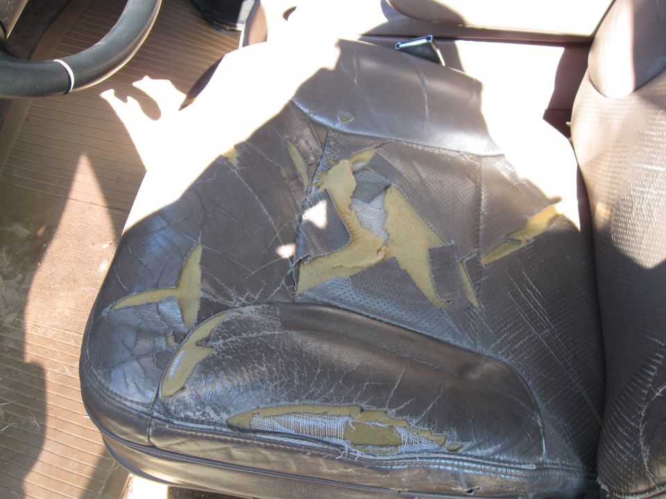 Brown leather car seat with large tears exposing yellowing foam and fabric