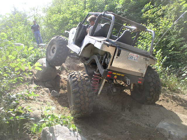 White doorless caged Jeep flexing over a rock ledge with front tire in the air