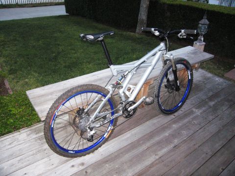 1986 Ford Bronco - A silver full-suspension mountain bike with blue rims rests on a wooden deck next to a bench.
