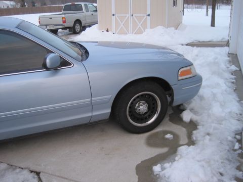 1999 Ford Crown Victoria - Light blue sedan in snow, with a white pickup truck and shed in the background.