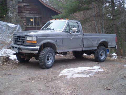 1979 Ford Bronco - This Ford F-350 pickup truck is parked on a dirt road in front of a rustic log cabin.