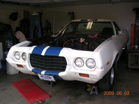 1972 Ford Ranchero - Front view of a 1972 Ford Ranchero in a garage, hood open, showing the engine bay and blue racing stripes.
