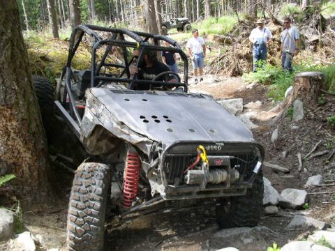 1979 Ford Bronco - A modified off-road buggy navigates a challenging wooded terrain with spectators watching.
