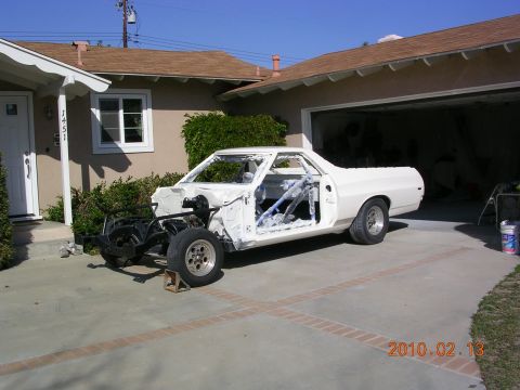 1972 Ford Ranchero - A white vehicle body is undergoing restoration, stripped down to its frame and placed on jack stands in a residential driveway.