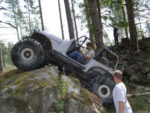 1979 Ford Bronco - A silver Jeep Wrangler TJ navigates a challenging rocky trail in a wooded area.