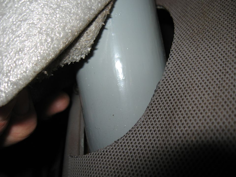 Hand lifting carpet backing to show a gray tubular roll bar passing through a cut hole