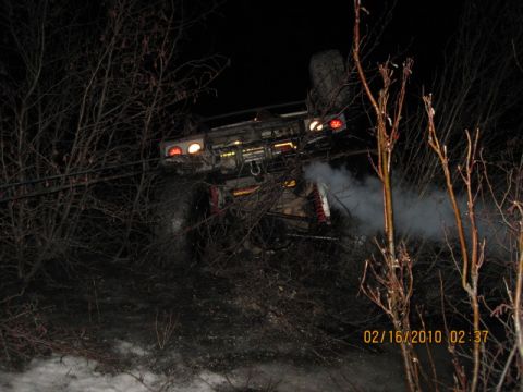 1990 Ford F-250 - A truck lies on its side in the dark, surrounded by trees and emitting a plume of smoke.