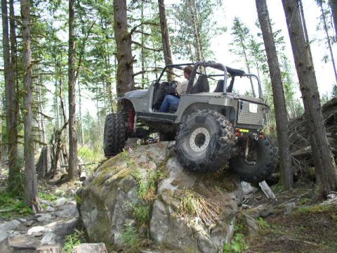 1979 Ford Bronco - A modified Jeep navigates a difficult rocky obstacle on a forest path.