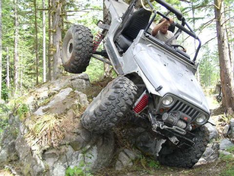 1979 Ford Bronco - A silver Jeep Wrangler navigates a rocky trail, with its front-right tire high in the air.
