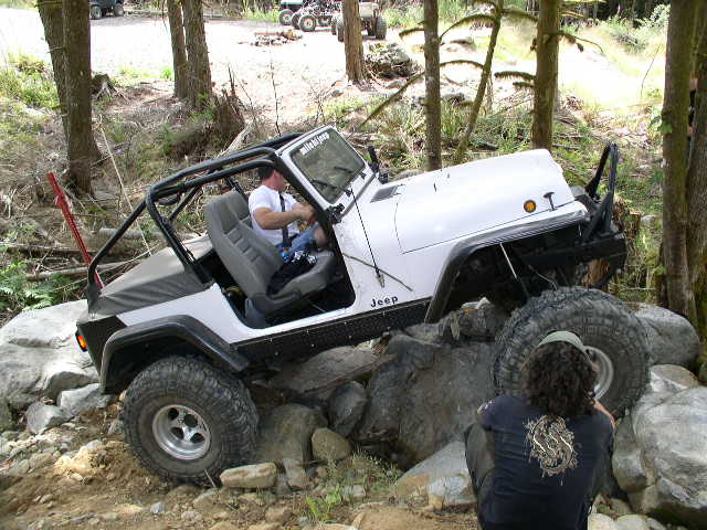 White topless Jeep Wrangler with roll cage crawling boulders as a spotter watches