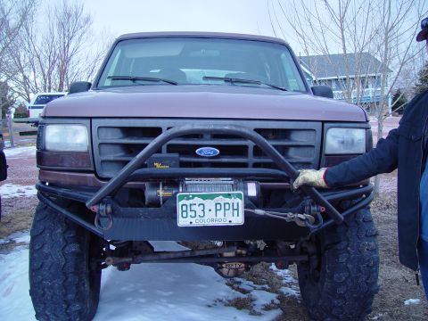 1993 Ford Bronco - A person's hand is on the brush guard of a lifted Ford Bronco parked in a snowy area.
