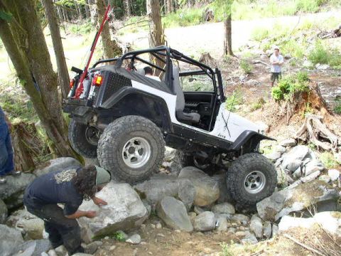 1979 Ford Bronco - A modified Jeep Wrangler tackles a challenging rocky terrain, with a spotter guiding its path.