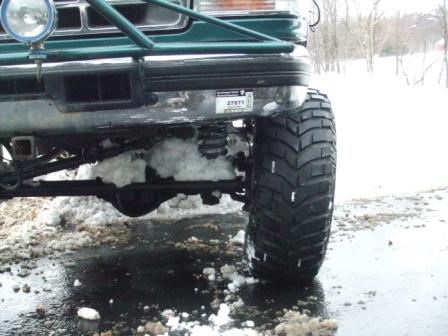 1996 Ford Bronco - Low front corner view of a lifted green Ford Bronco with snow packed into the front axle and suspension, showing the tube bumper with a rou…