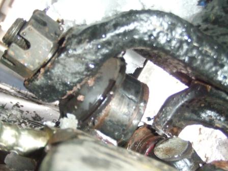 1996 Ford Bronco - Extreme close-up of a greasy, snow-dusted steering knuckle area on a solid front axle, showing a cracked and broken cast component around t…