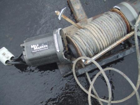 1996 Ford Bronco - A removed Mile Marker winch lying on wet pavement, its rusty drum wound with synthetic rope and loose coils trailing off to the side. The m…