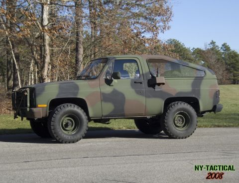 1988 Ford Bronco - A woodland camouflage (green, brown, black) two-door SUV shown in side profile, lifted on military-style steel wheels with off-road tires a…