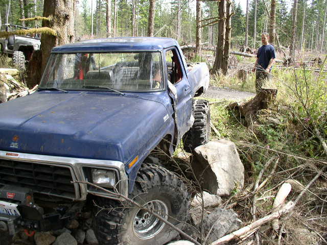 Blue doorless 1970s Ford Bronco with winch over rocks in a logged forest