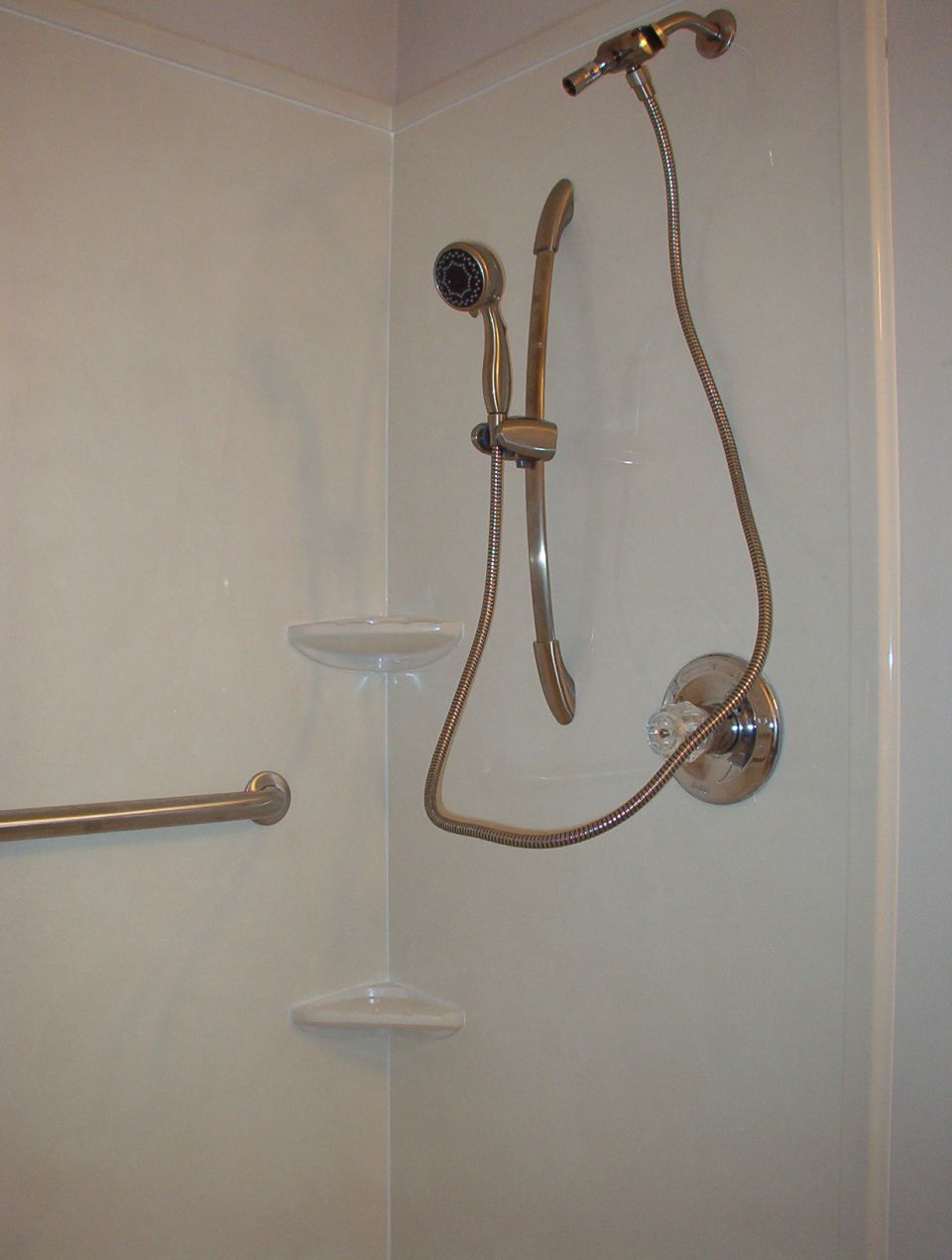 Handheld shower head on slide bar with chrome valve trim in a white fiberglass shower stall
