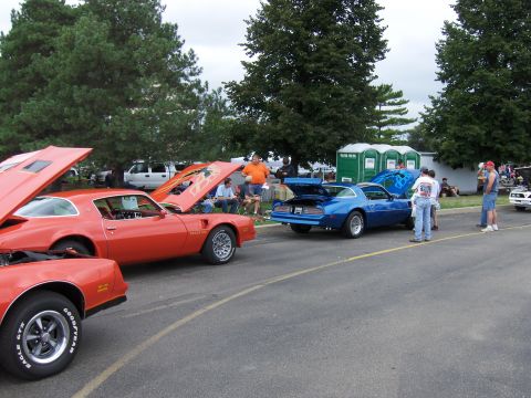 1978 Pontiac Trans Am - Two Pontiac Trans Ams, one orange and one blue, are displayed with their hoods open at an outdoor event.