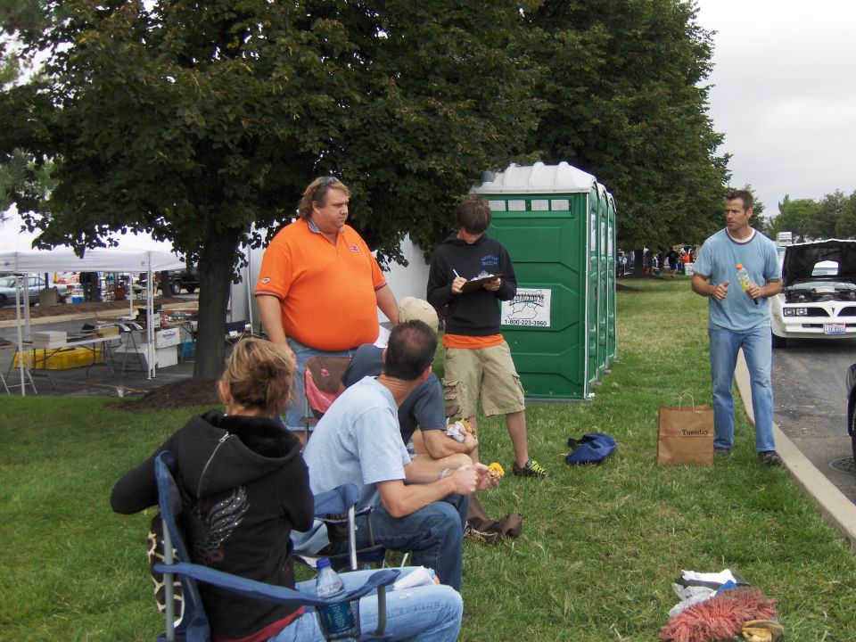 1978 Pontiac Trans Am with hood open, parked near portable toilets and people