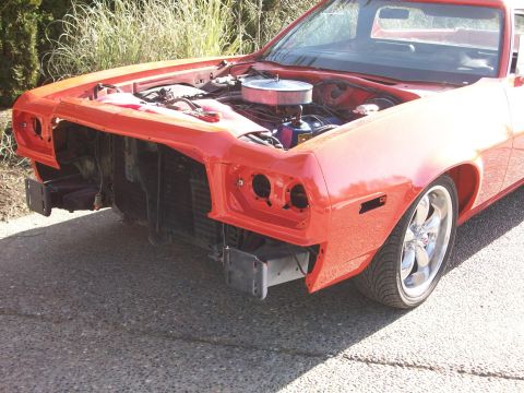 1973 Ford Ranchero - Red Ford Ranchero mid-reassembly outdoors with the grille, headlights and bumper removed, exposing the core support, radiator and bumper br…