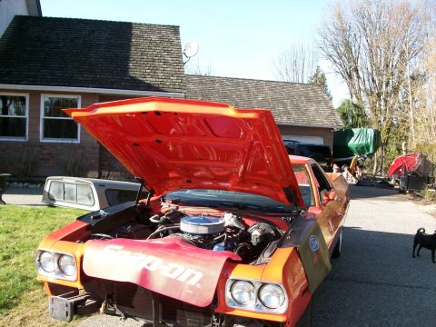 1973 Ford Ranchero - The front of an orange vehicle is shown with its hood open, revealing the engine bay and Snap-on fender covers.