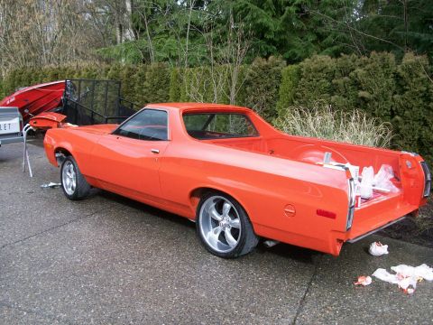 1973 Ford Ranchero - Rear three-quarter view of a freshly painted orange-red Ford Ranchero coupe-utility mid-reassembly on a driveway, with the tailgate down, c…