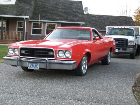 1973 Ford Ranchero - Red Ford Ranchero coupe utility on a driveway in front of a house, shot from the front three-quarter with FORD lettering on the hood lip, q…