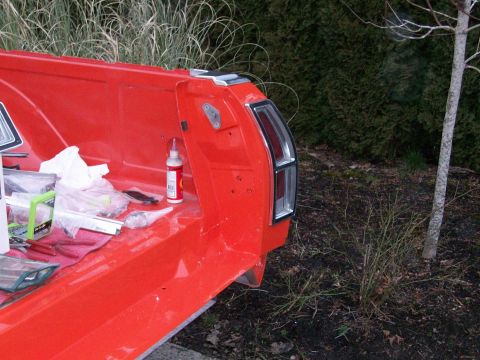 1973 Ford Ranchero - Rear quarter of a freshly painted red coupe-utility bed during trim reassembly, with the vertical chrome-bezel taillight installed and body…