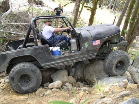 1979 Ford Bronco - Driver maneuvers a black Jeep CJ over large rocks during an off-road excursion.
