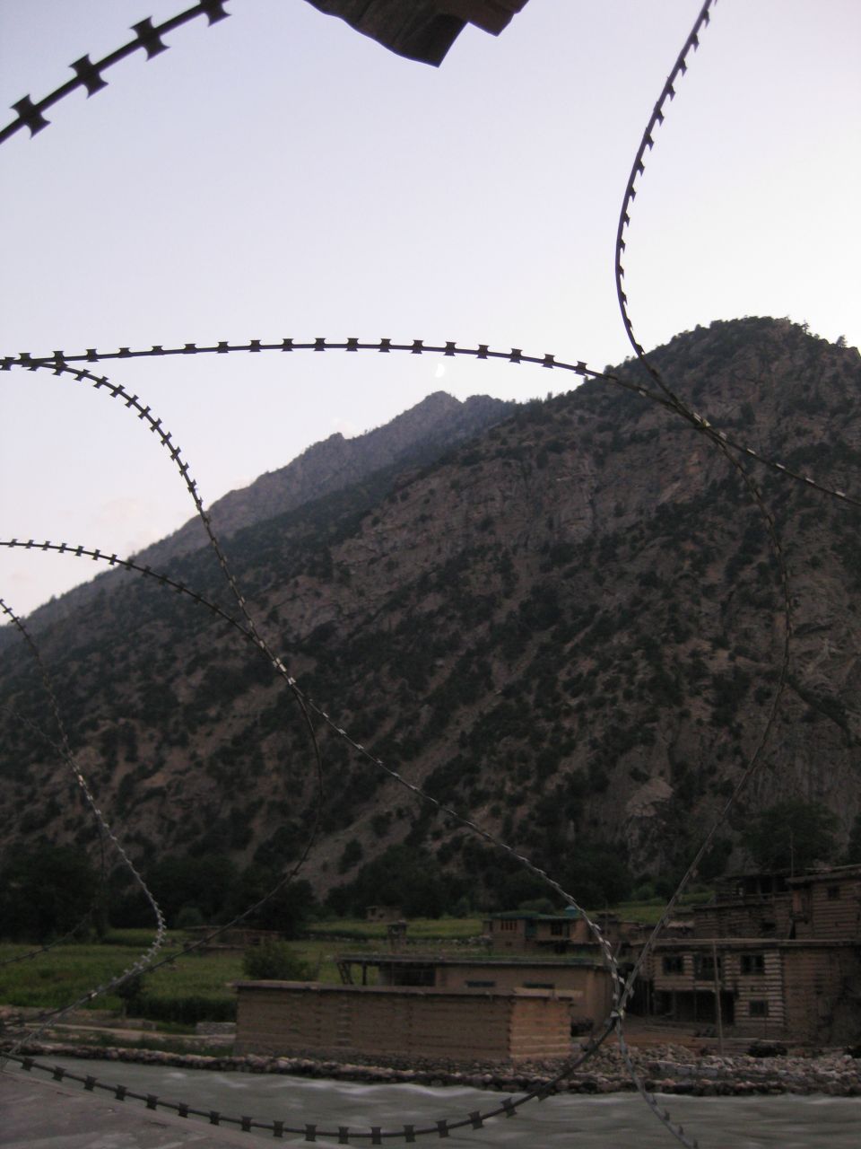 barbed wire in foreground with mountains and buildings in background