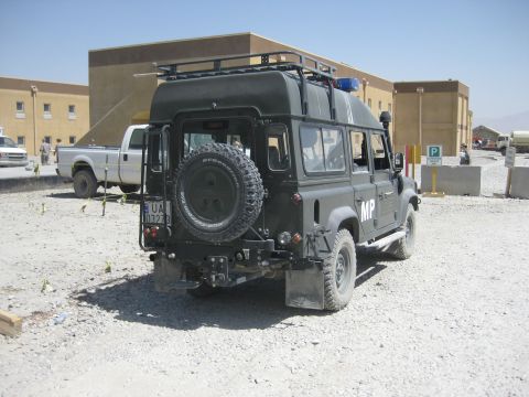 2003 Jeep Wrangler - A military police Land Rover Defender is parked in a lot with buildings and another vehicle nearby.