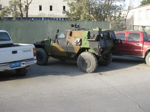 2003 Jeep Wrangler - A camouflage-painted 4x4 armored military scout car parked on cracked pavement, side view showing a roof-mounted machine gun, small armored…