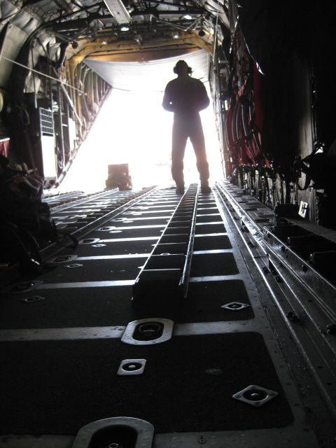 2003 Jeep Wrangler - View from inside a cargo plane looking towards the open rear ramp, with a person standing silhouetted against the bright daylight outside.