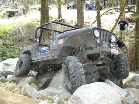 1979 Ford Bronco - Jeep CJ-7 tackling a challenging rock obstacle in a wooded area.