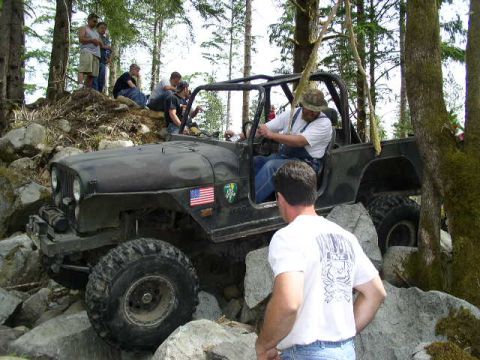 1979 Ford Bronco - A group of people watch as a Jeep CJ-7 navigates a rocky trail in a wooded area.