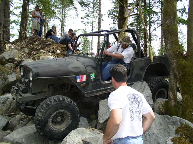Jeep CJ-7 driving over rocks with people watching