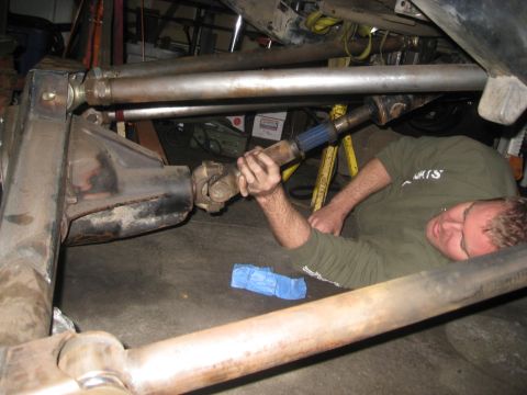 1994 Jeep YJ - A mechanic is seen working on the driveshaft and differential of a vehicle, likely during a repair or modification.