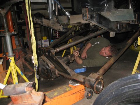 1994 Jeep YJ - A mechanic works on the suspension and axle of a vehicle that is raised on jack stands.