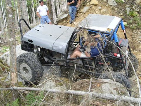1979 Ford Bronco - An off-road buggy with a custom roll cage navigates a challenging rocky trail in a wooded area.